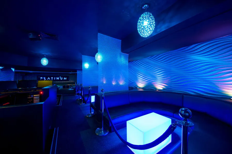 VIP seating areas with wavy wall panels and illuminated central table in vibrant nightlife venue.