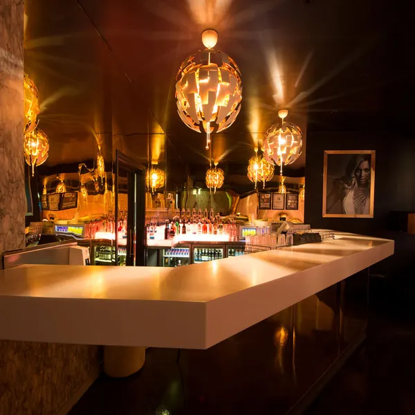 Close-up of the gold-toned bar area with mirrored panels and geometric pendant lights in a high-end nightclub.