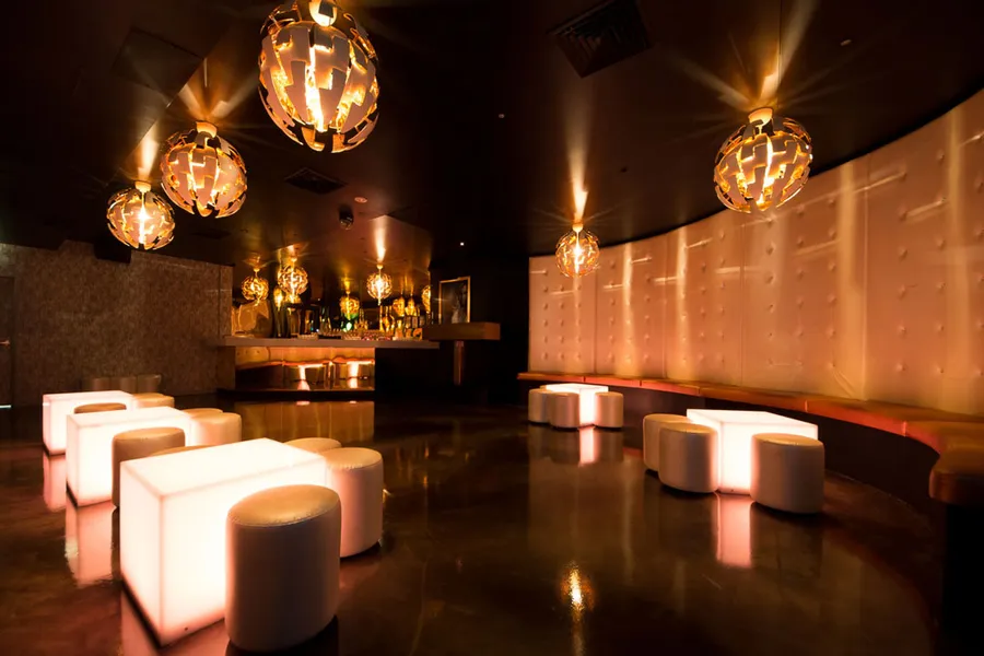 Elegant view of the gold-themed room in nightclub, featuring white upholstered seating and modern illuminated tables.