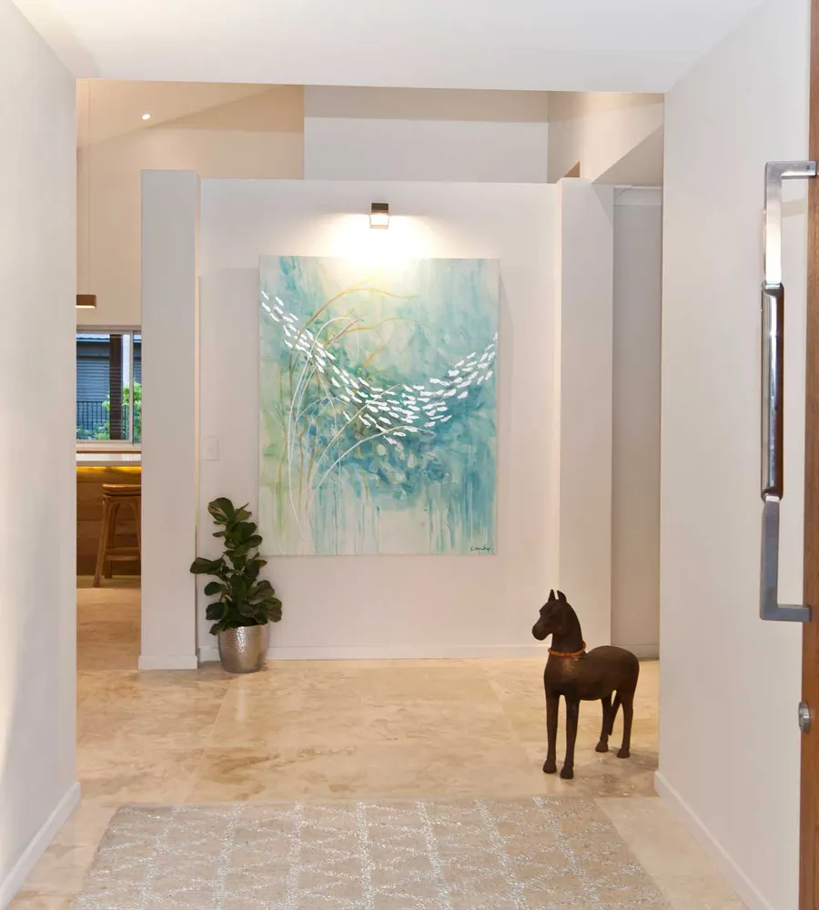 A bright and spacious entrance featuring a wall art at the end, white walls and travertine marble flooring