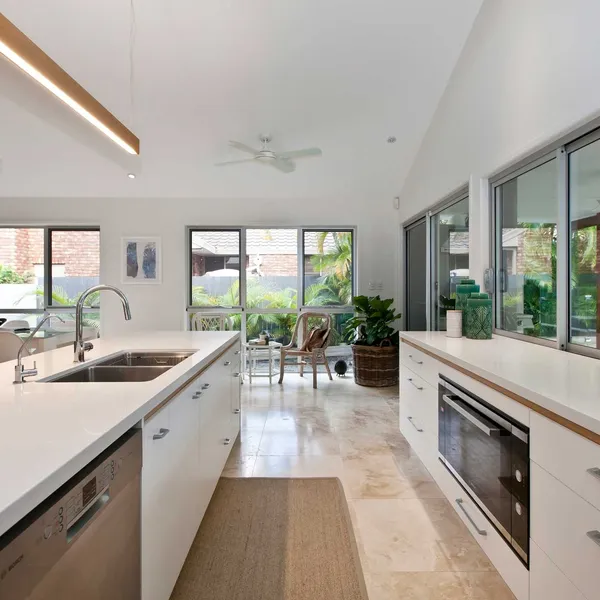 Kitchen viewpoint capturing the connection to the dining area, showing the synergy of natural stone flooring and timber accents Modern kitchen showcasing the open scullery, white bench space, and the clean design lines