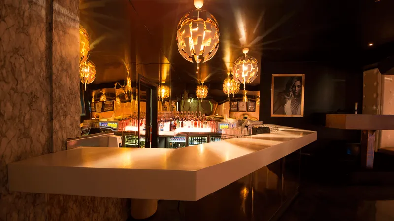 An elegant bar with dark gold and white lighting, featuring a cyclorama, arabesque design, wimmelbilder art, glass materials, christcore, and neue sachlichkeit style.