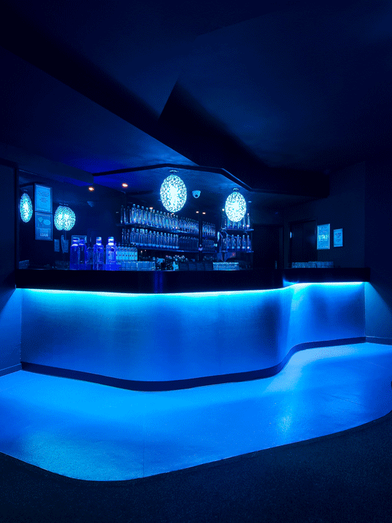 A dimly lit bar bathed in soothing blue light, reflecting the tranquil blend of sea and land, enhancing the sensory experience.