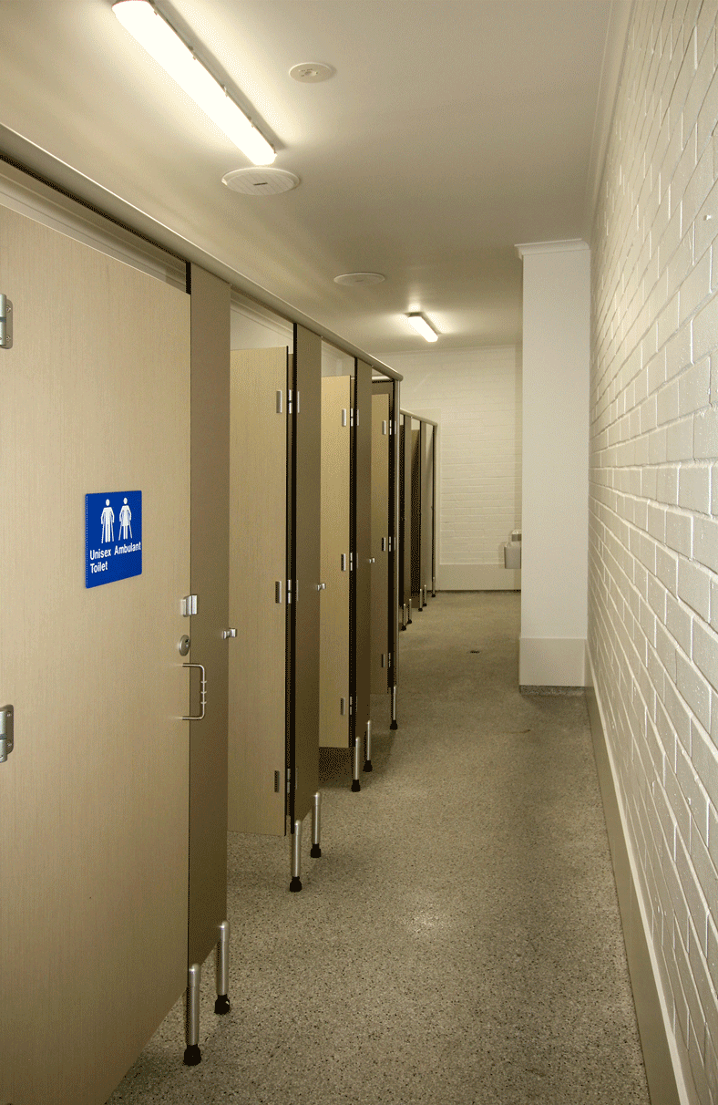 An interior view of a well-maintained sports facility showing the shower and toilet areas, including an ambulant toilet and shower cubicles. Clean, non-slip flooring and painted brick walls reflect the high standards of facility maintenance.