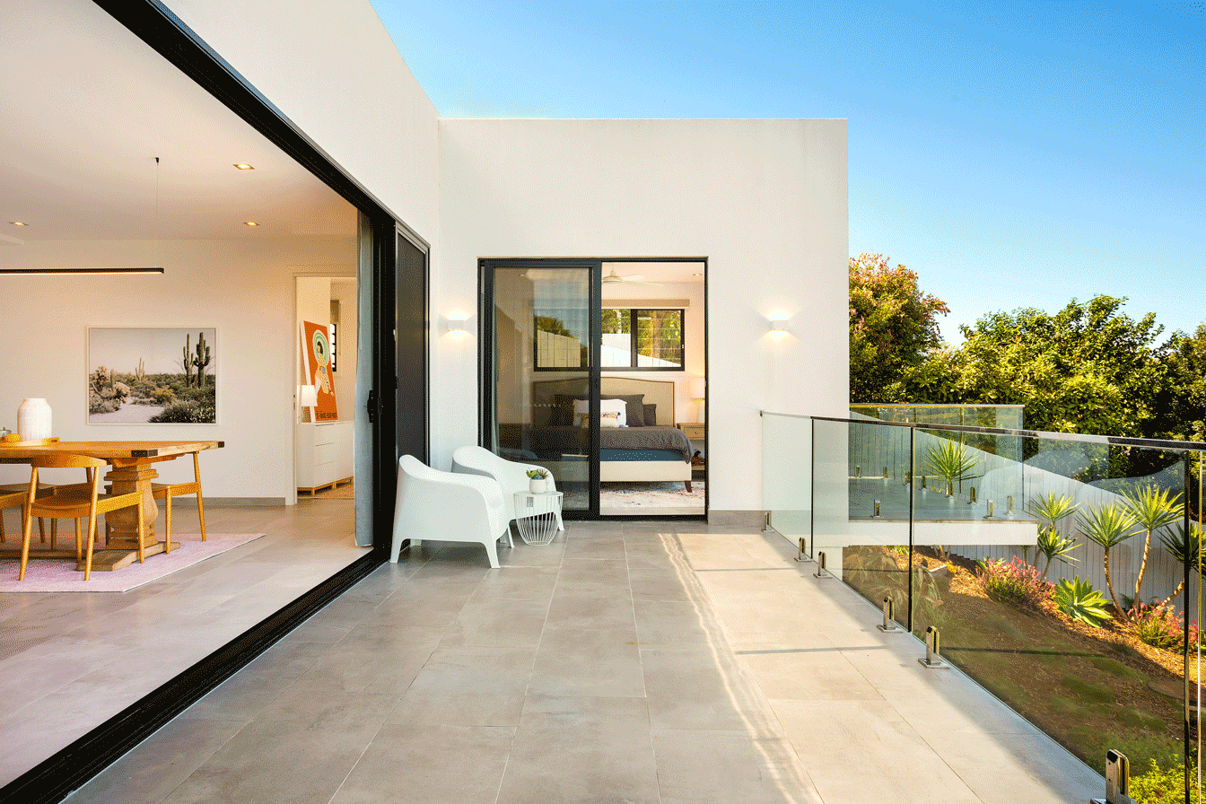 Modern white residential house with a large balcony, sliding glass doors, reflecting a design aesthetic of playful minimalism and timeless elegance, with an emphasis on solarising mastery and light-filled spaces.