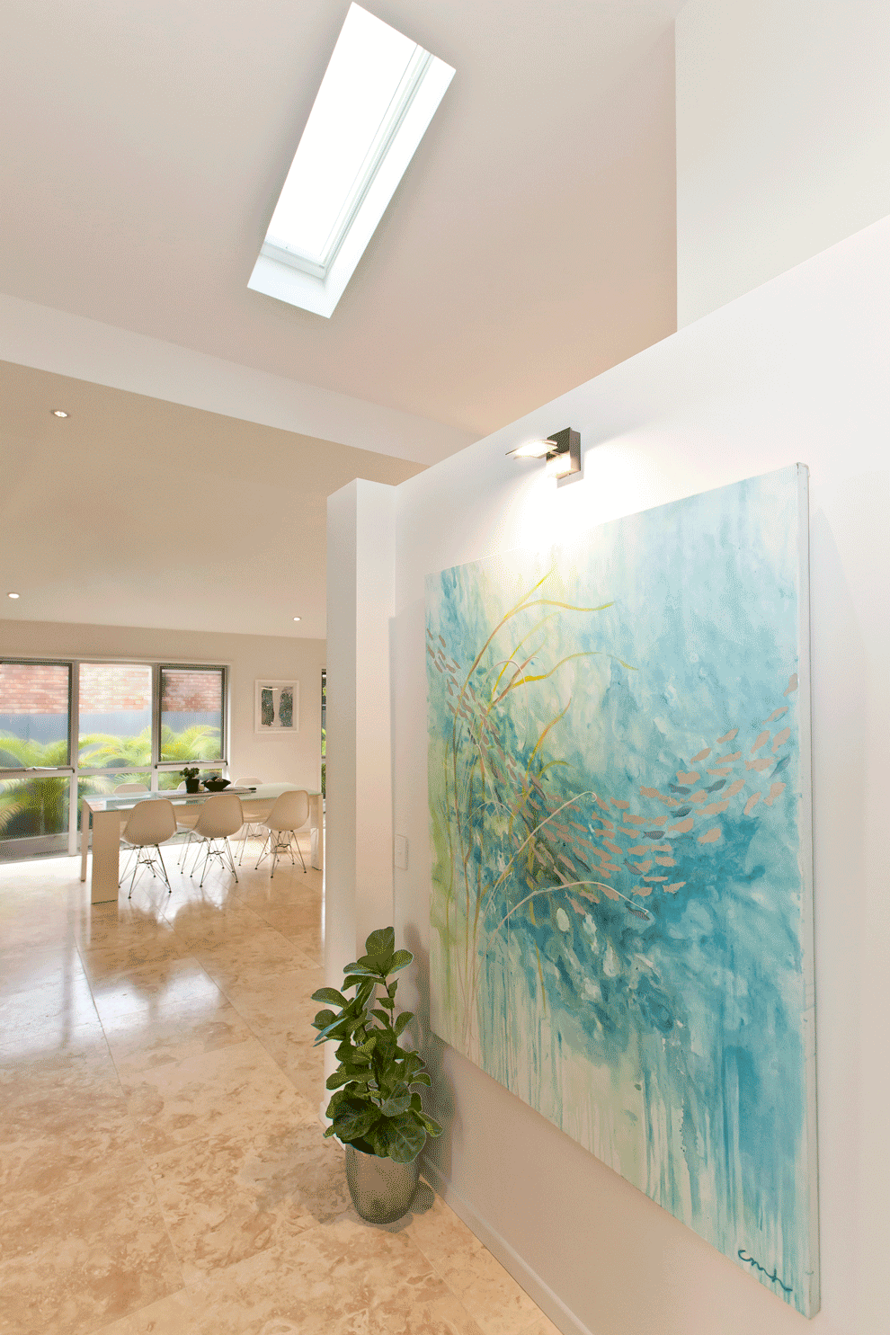 A modern interior showcasing a large canvas painting on a wall, suffolk coast views, light aquamarine and green textiles, and travertine tiled floor.