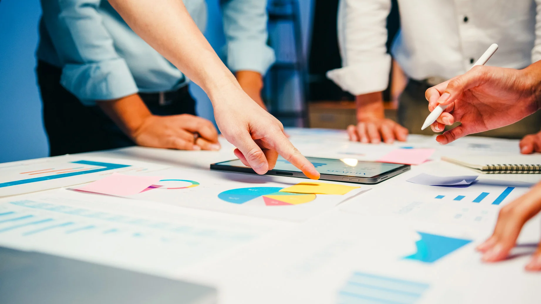 Project Managers pointing at schedules on a table with a tablet and graphs